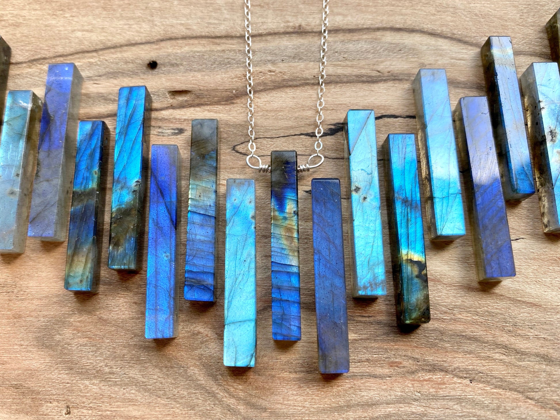 May include: A silver chain necklace with a pendant made of multiple blue labradorite stones arranged in a vertical row. The stones are rectangular and have a iridescent sheen.