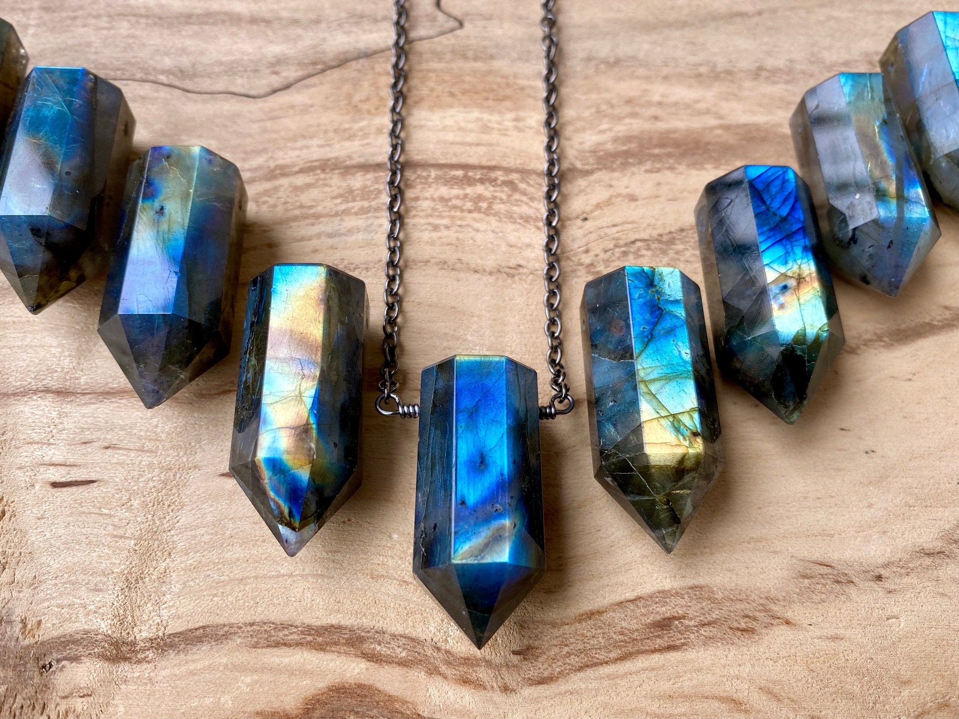 May include: A silver chain necklace with seven iridescent labradorite crystal points. The crystal points are faceted and have a blue, green, and gold color.